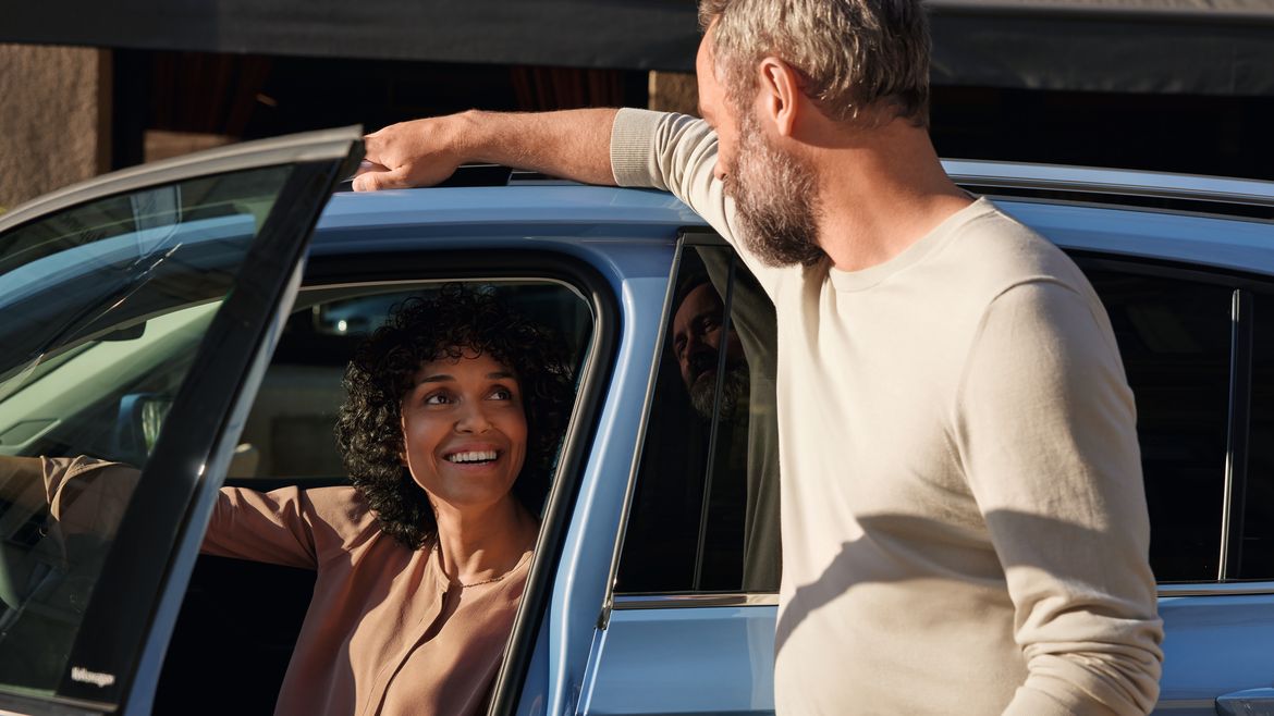 Mann redet mit einer Frau, die am Fahrersitz eines blauen VW T-Cross sitzt