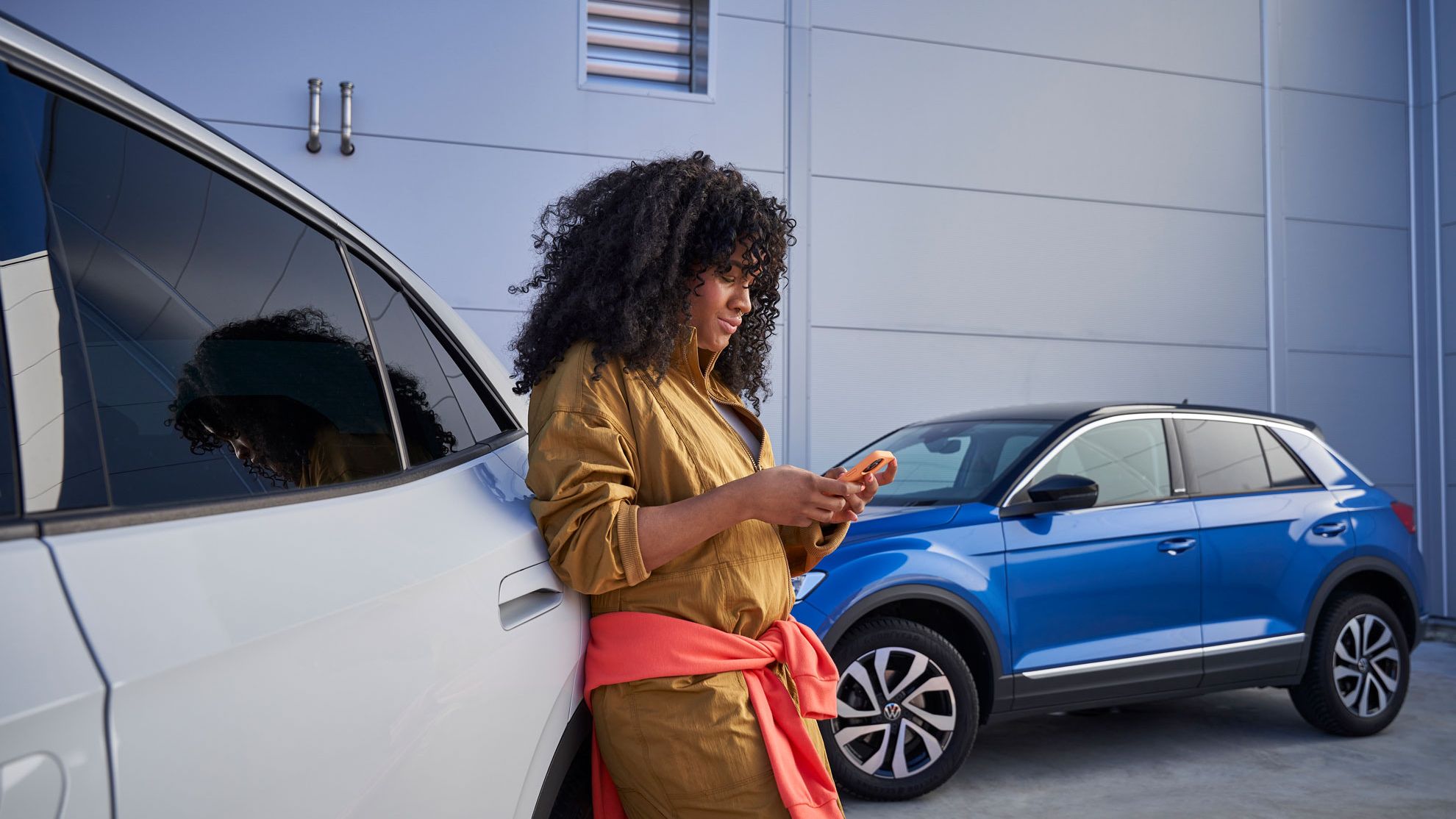 Eine Frau steht angelehnt an einem Volkswagen und schaut dabei auf ihr Smartphone