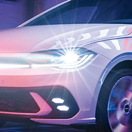 Ein weißer VW Polo GTI fährt in einer Halle mit eingeschalteten LED-Matrix-Scheinwerfern und Lichtleiste in der Front