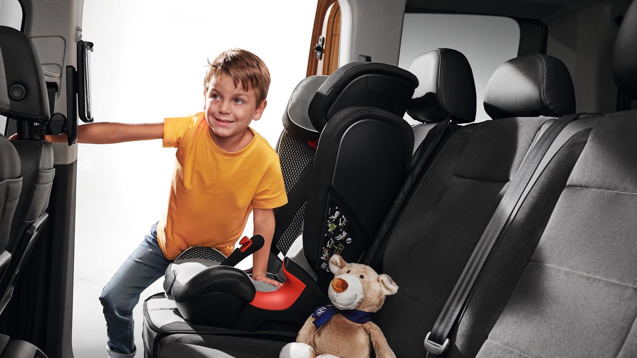 Kind steigt in einen VW Caddy ein und will sich in den Kindersitz setzen