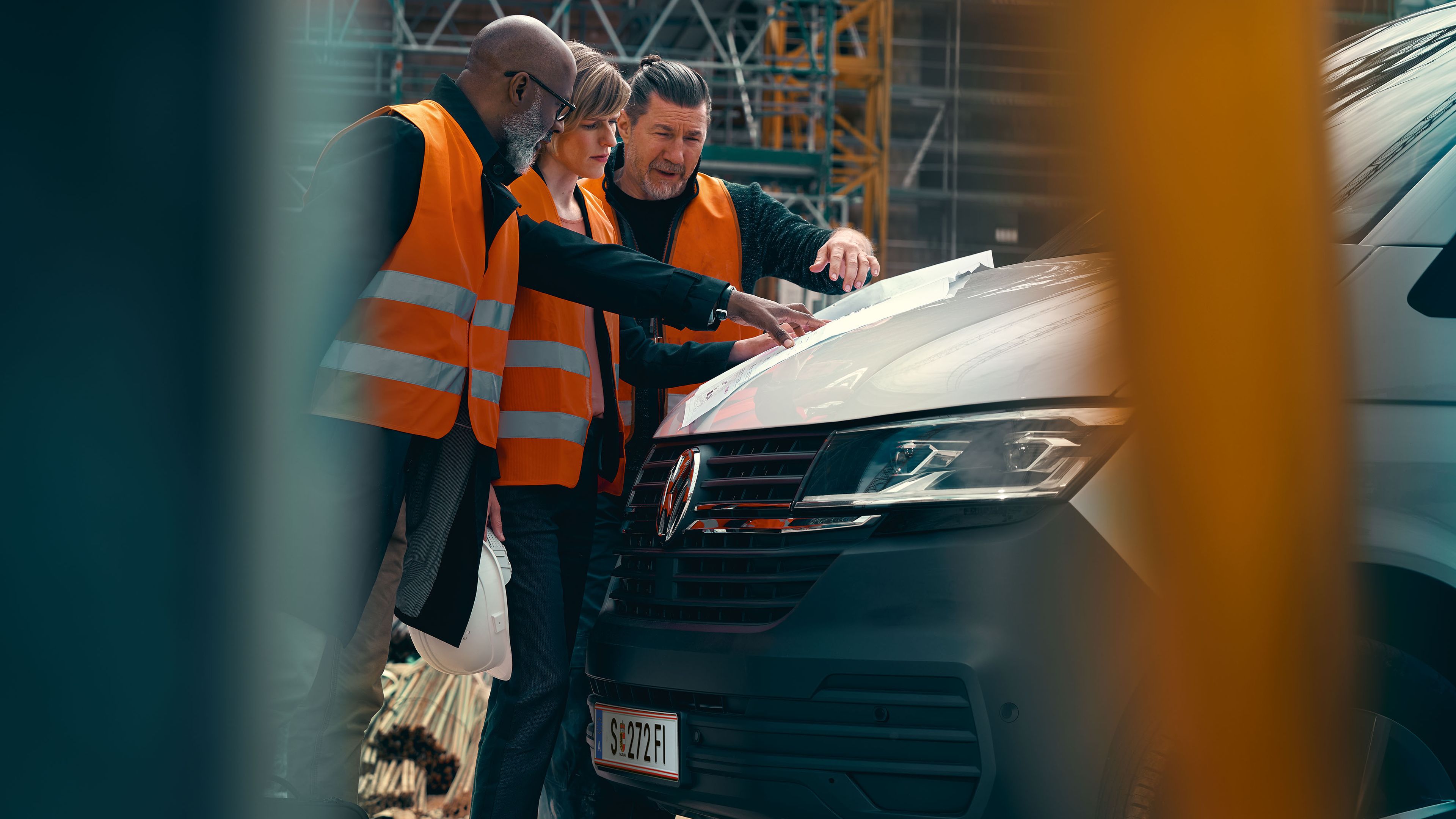 Zu sehen ist ein VW Transporter 6.1 Pritschenwagen auf einer Baustelle. Drei Arbeiter besprechen gerade etwas. 