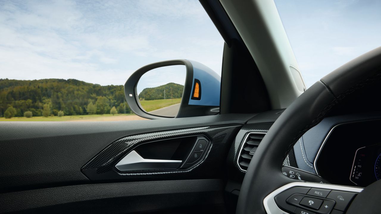 Nahaufnahme des Seitenspiegels eines blauen VW T-Cross vor Wald-Landschaft.