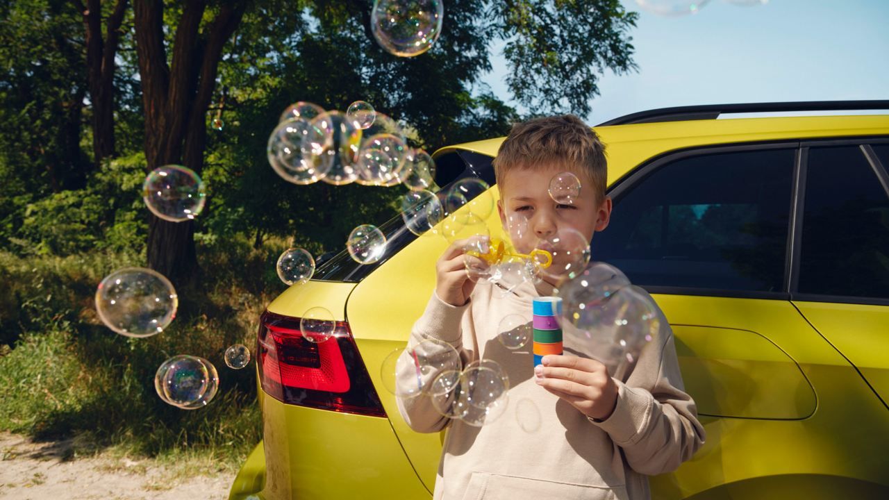 Kind bläst Seifenblasen vor VW Golf Variant