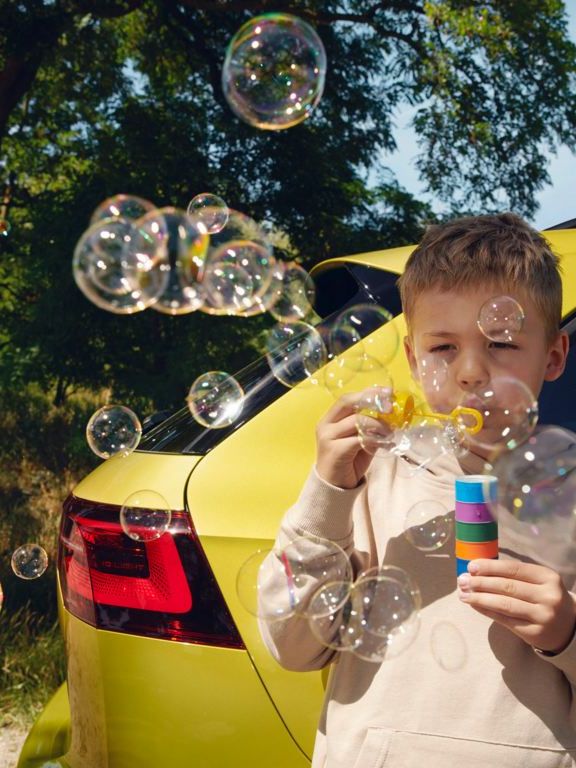 Kind bläst Seifenblasen vor VW Golf Variant