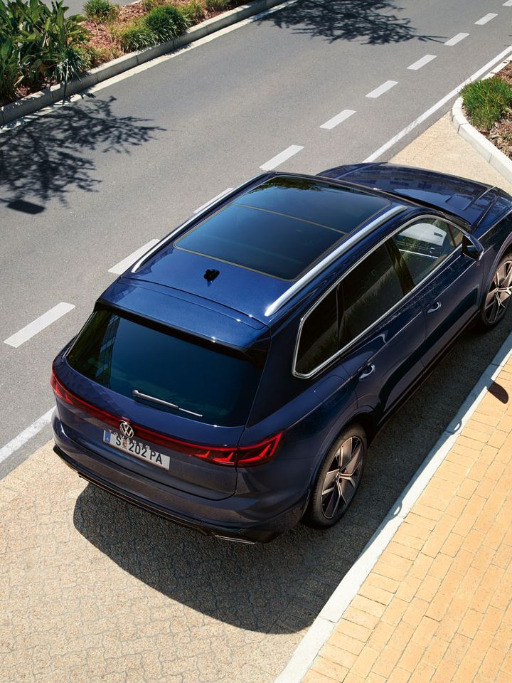 Ein VW Touareg R-Line parkt am Straßenrand, Ansicht von schräg oben auf das Heck und Panoramaglasdach.