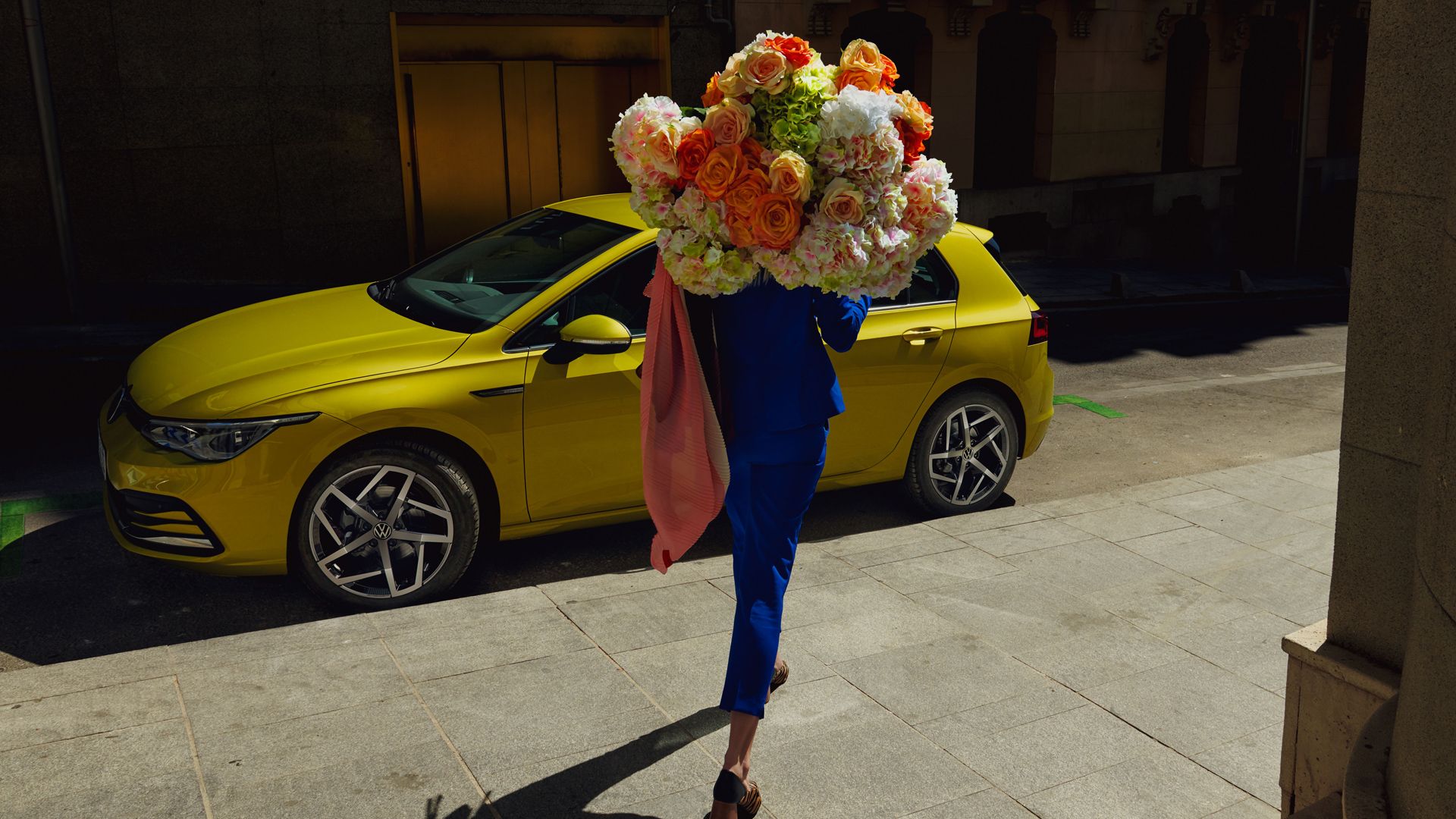 Zu sehen ist eine Frau die gerade auf den neuen VW Golf zugeht und einen Blumenstrauß hält. 