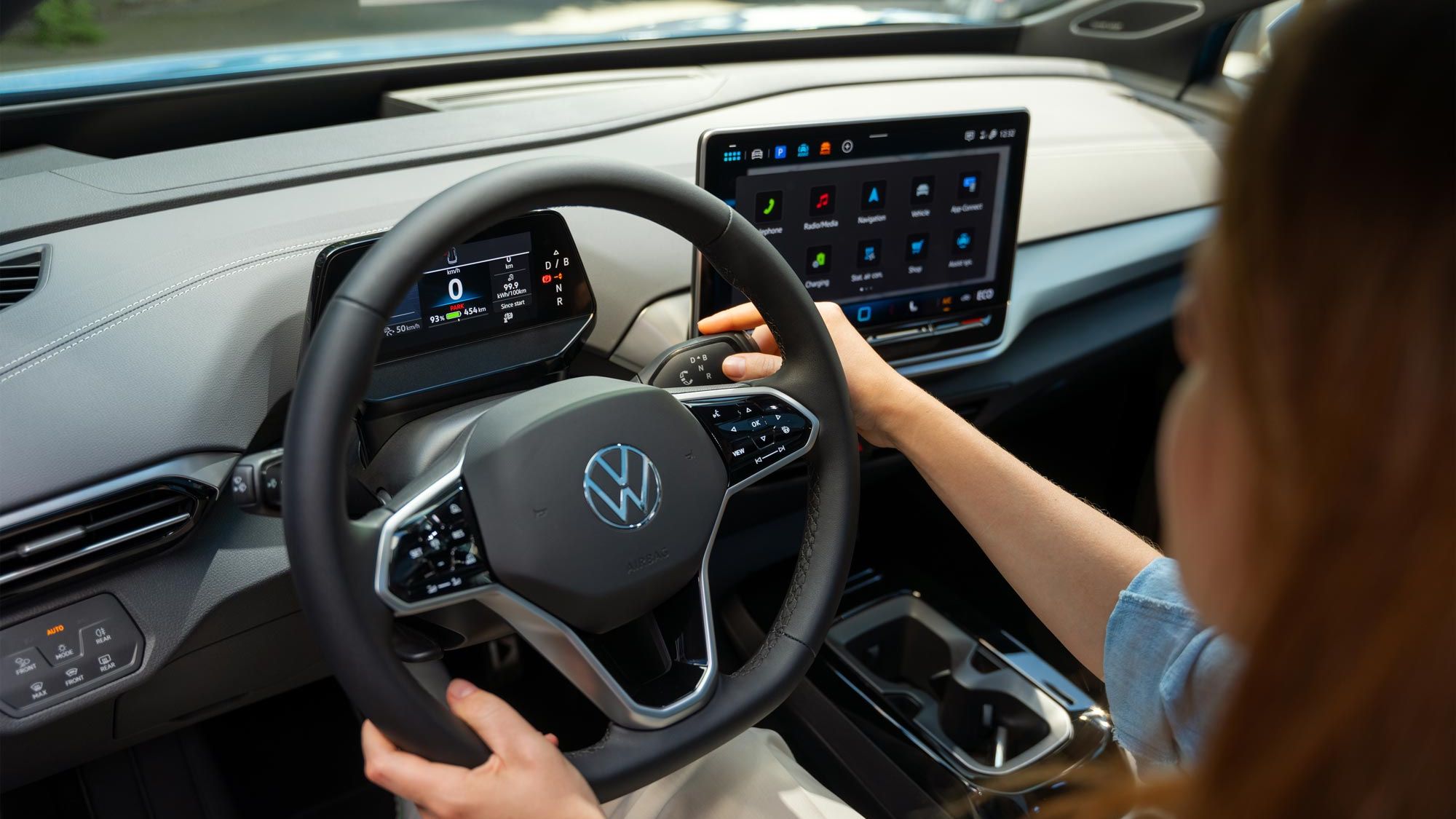 Innenansicht eines stehenden VW ID.4. Eine Frau sitzt auf dem Fahrersitz, ihre rechte Hand bedient den Schalthebel am Lenkrad.